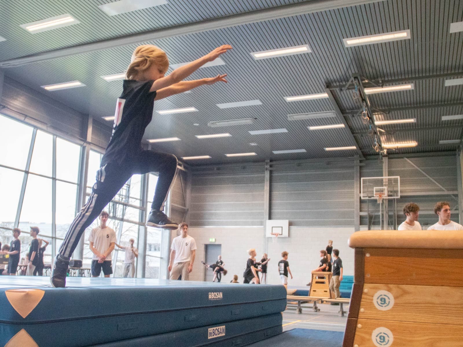 Een jonge freerunner oefent een sprong op een dikke valmat onder begeleiding van trainers